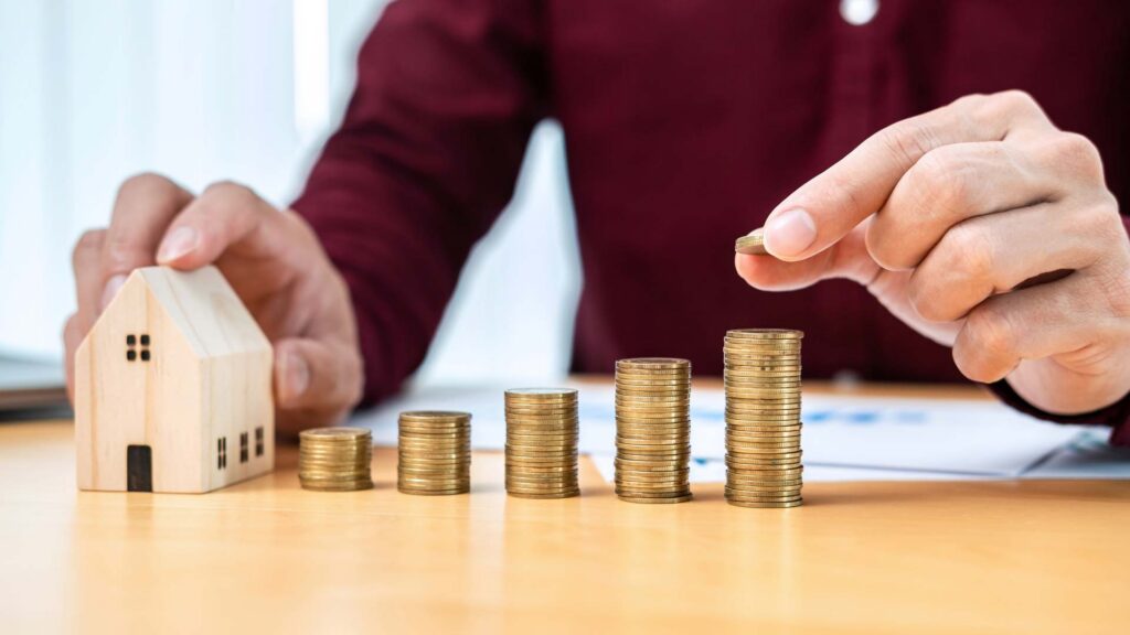 mann_stapelt_muenzen_neben_haus